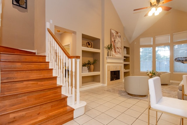 tiled living room with lofted ceiling, built in shelves, ceiling fan, and a tiled fireplace