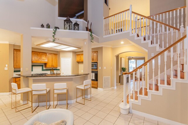 kitchen with a towering ceiling, backsplash, light tile patterned floors, dark stone countertops, and a breakfast bar area