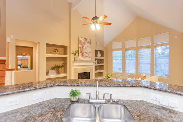 kitchen with built in shelves, ceiling fan, sink, a tile fireplace, and high vaulted ceiling