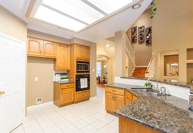 kitchen with stainless steel microwave, sink, kitchen peninsula, oven, and dark stone counters