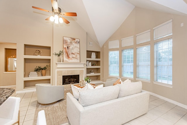 tiled living room featuring built in shelves, ceiling fan, plenty of natural light, and a tiled fireplace