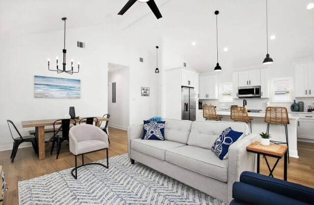 living room with beamed ceiling, ceiling fan with notable chandelier, high vaulted ceiling, and light hardwood / wood-style flooring