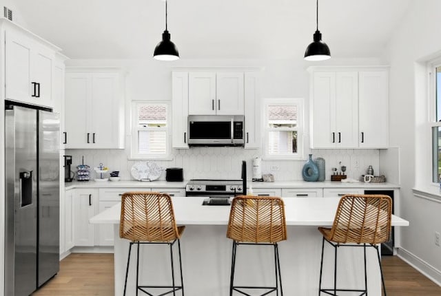 kitchen featuring white cabinets, stainless steel appliances, a kitchen island with sink, and hanging light fixtures