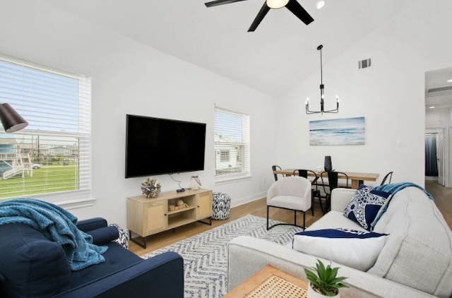 living room with ceiling fan with notable chandelier, high vaulted ceiling, and light hardwood / wood-style flooring