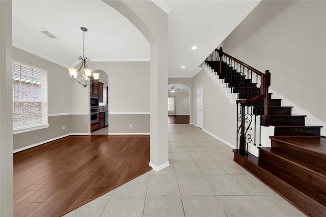 foyer with ceiling fan with notable chandelier, light tile patterned flooring, and crown molding