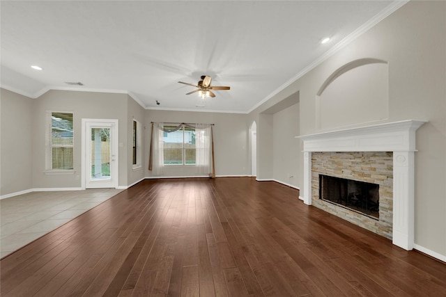 unfurnished living room with ceiling fan, dark hardwood / wood-style floors, a stone fireplace, and crown molding