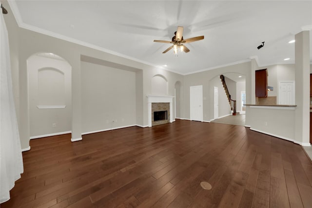 unfurnished living room featuring dark wood-type flooring, a stone fireplace, ceiling fan, and crown molding