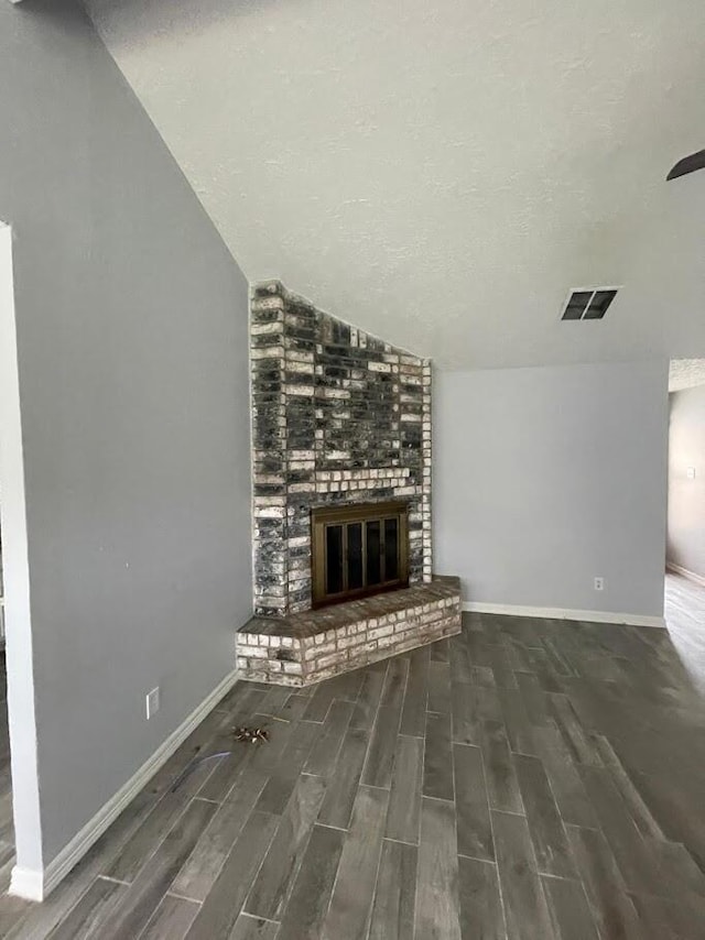 unfurnished living room featuring vaulted ceiling, a textured ceiling, and a brick fireplace