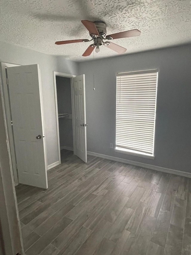 unfurnished bedroom with ceiling fan, dark hardwood / wood-style flooring, a textured ceiling, and multiple windows