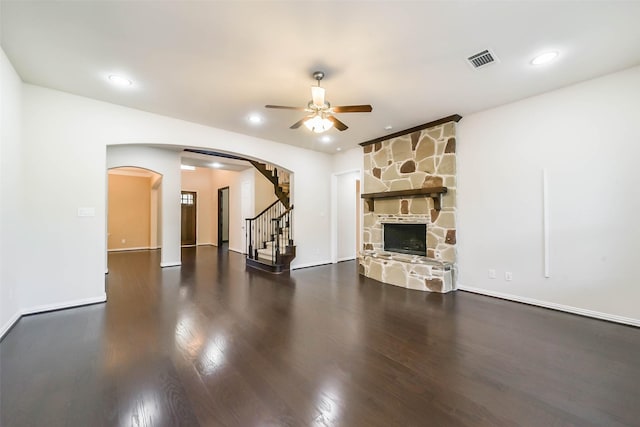 unfurnished living room featuring ceiling fan, dark hardwood / wood-style flooring, and a stone fireplace