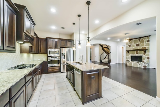 kitchen featuring appliances with stainless steel finishes, dark brown cabinetry, sink, pendant lighting, and a center island with sink