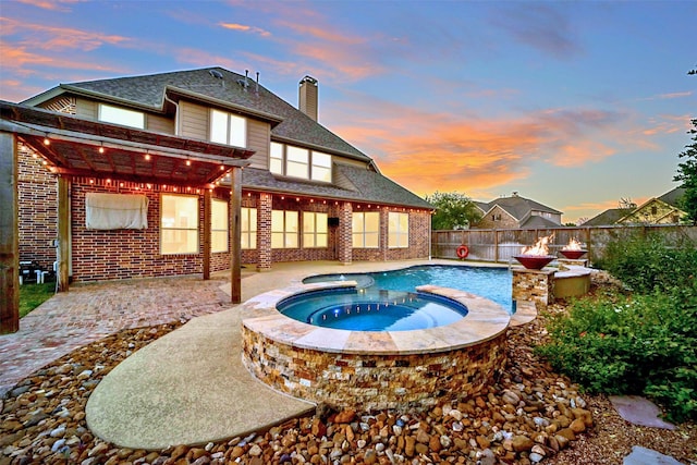 pool at dusk with an in ground hot tub and a patio area