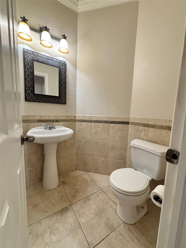 bathroom featuring tile patterned floors, toilet, crown molding, and tile walls