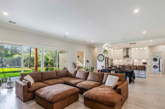 living room featuring ornamental molding, light hardwood / wood-style floors, and stacked washer / drying machine