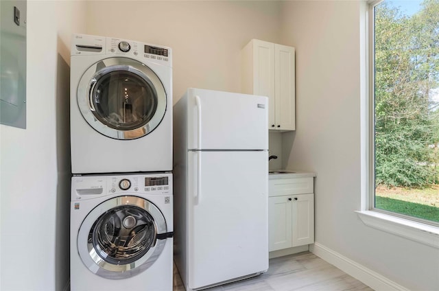 washroom with stacked washer / drying machine, cabinets, and sink