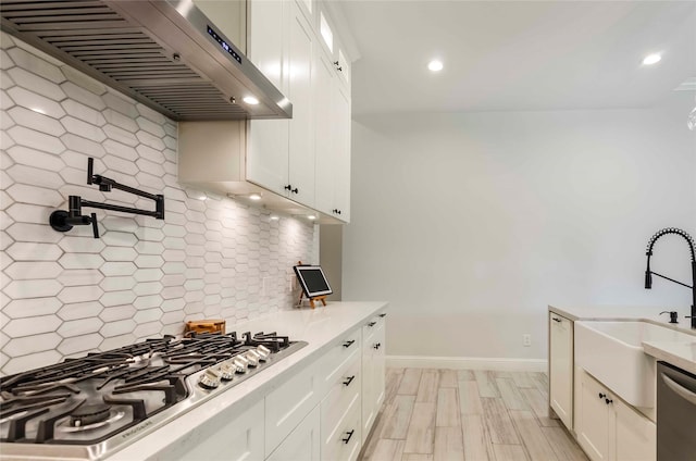 kitchen featuring decorative backsplash, appliances with stainless steel finishes, white cabinetry, and wall chimney exhaust hood