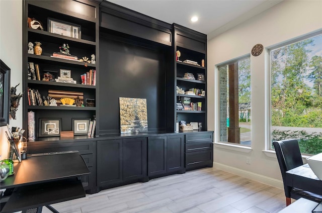 home office featuring built in shelves, a healthy amount of sunlight, and light hardwood / wood-style flooring