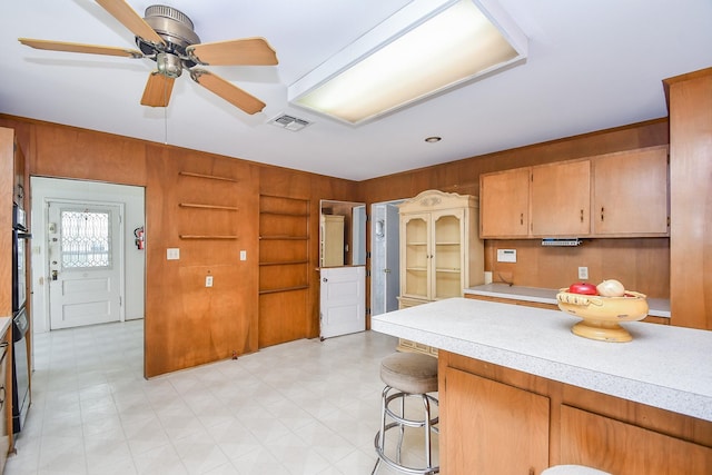 kitchen with ceiling fan, a breakfast bar, and wooden walls