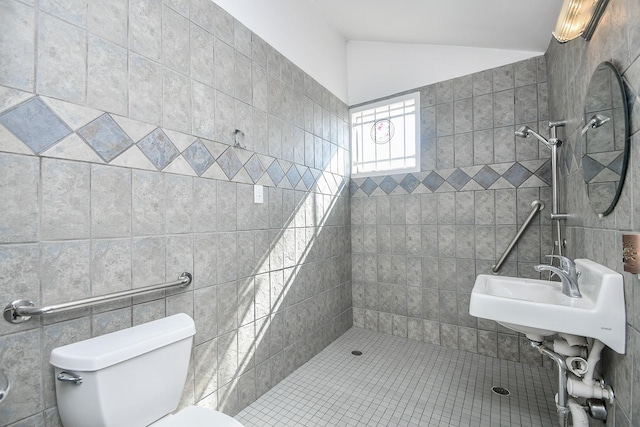 bathroom with a tile shower, toilet, lofted ceiling, and sink