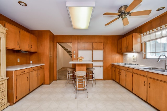 kitchen with ceiling fan, a kitchen bar, white gas stovetop, and sink