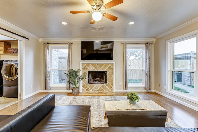 living room with light wood-type flooring, washer / clothes dryer, crown molding, and a tile fireplace