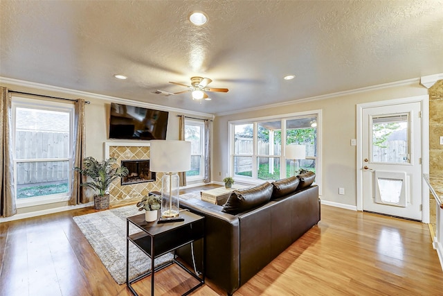 living room featuring a tiled fireplace, ceiling fan, and crown molding