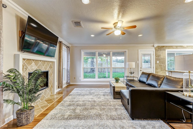 living room featuring light wood-type flooring, a textured ceiling, ceiling fan, crown molding, and a fireplace