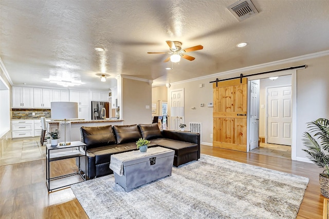 living room featuring a barn door, light hardwood / wood-style floors, a textured ceiling, and ornamental molding