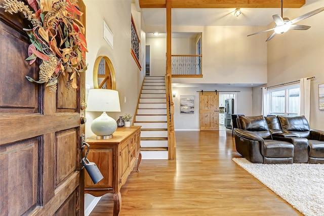 living room featuring ceiling fan, a barn door, a towering ceiling, beamed ceiling, and light hardwood / wood-style floors