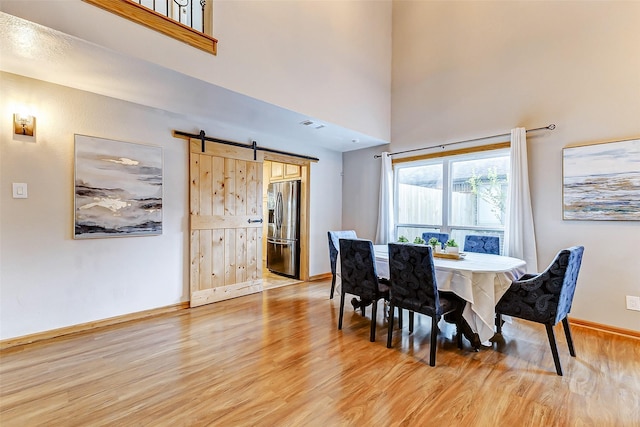 dining room with a barn door, a towering ceiling, and light hardwood / wood-style floors