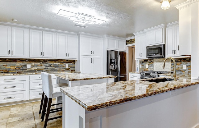 kitchen featuring sink, light stone counters, refrigerator with ice dispenser, backsplash, and a kitchen island