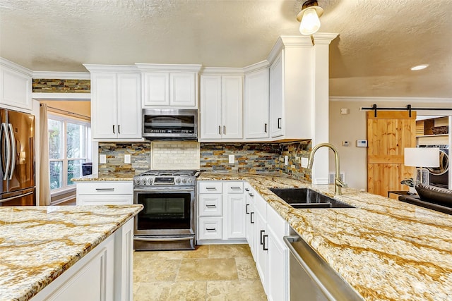 kitchen featuring white cabinetry, sink, tasteful backsplash, a barn door, and appliances with stainless steel finishes