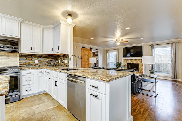 kitchen with sink, a barn door, appliances with stainless steel finishes, white cabinetry, and kitchen peninsula