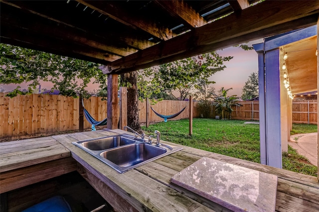 patio terrace at dusk with a lawn, a wooden deck, and sink