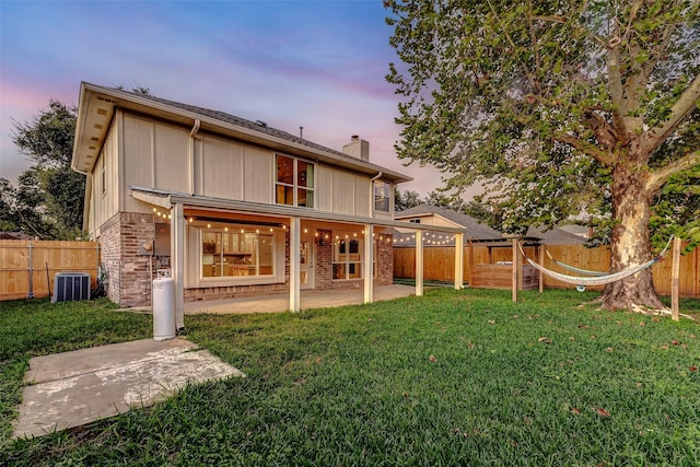 back house at dusk with a yard, central AC, and a patio area