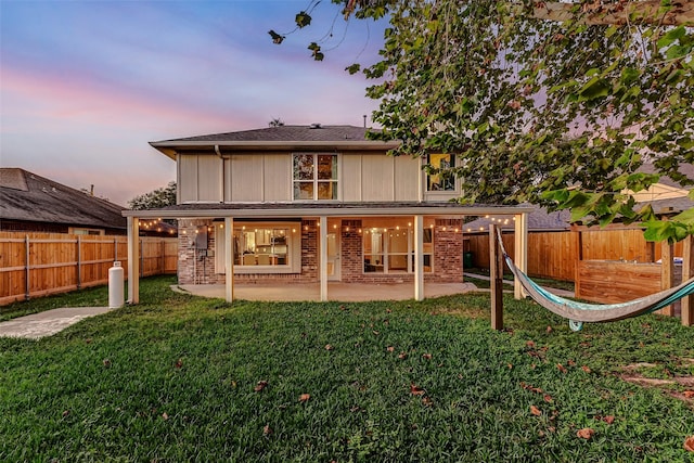 back house at dusk with a patio area and a lawn