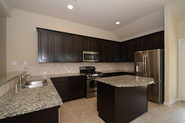 kitchen with light stone countertops, a center island, sink, stainless steel appliances, and vaulted ceiling