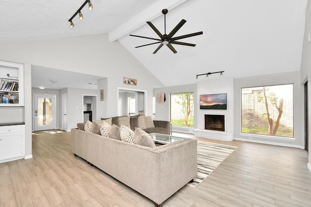 living room with beam ceiling, a wealth of natural light, a large fireplace, and light hardwood / wood-style floors