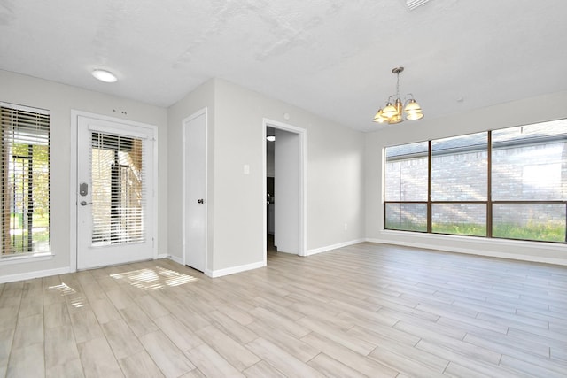 unfurnished room with a chandelier, light wood finished floors, and baseboards