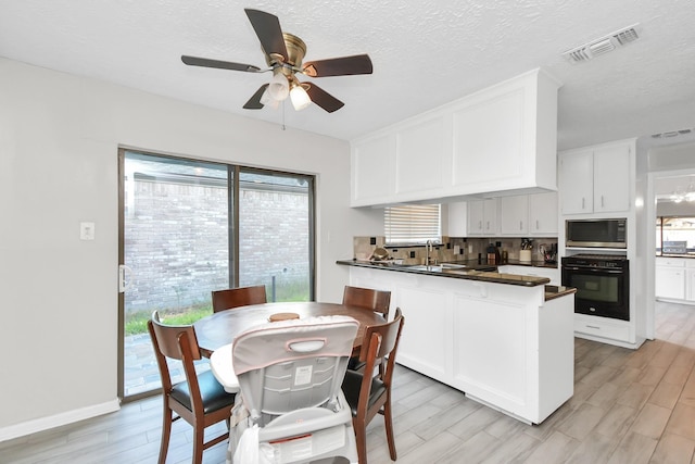 kitchen with stainless steel microwave, backsplash, oven, kitchen peninsula, and white cabinetry