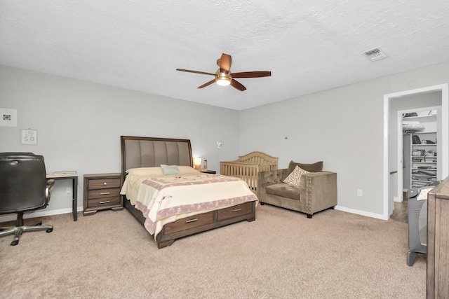 carpeted bedroom with a walk in closet, a textured ceiling, and ceiling fan