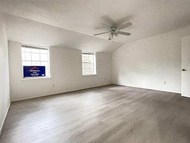 empty room with ceiling fan, vaulted ceiling, and light hardwood / wood-style floors