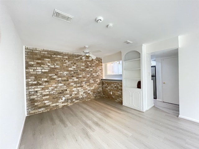 empty room featuring brick wall, ceiling fan, built in shelves, and light hardwood / wood-style flooring