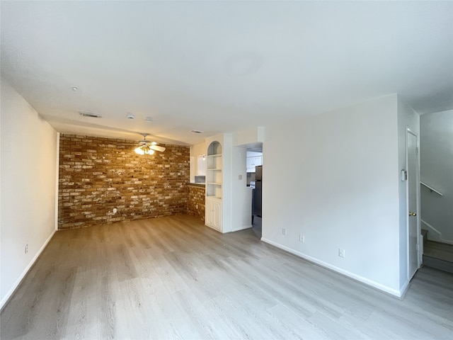 unfurnished living room with brick wall, light wood-type flooring, and ceiling fan