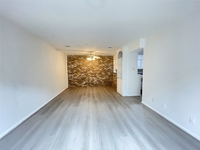 empty room with brick wall, light wood-type flooring, and ceiling fan