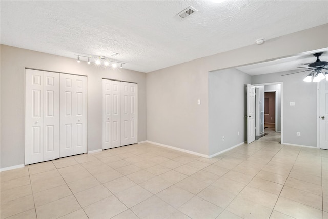 unfurnished bedroom with a textured ceiling, ceiling fan, light tile patterned floors, and two closets