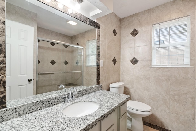 bathroom with vanity, toilet, tile walls, and a shower with shower door