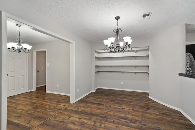 unfurnished dining area with a textured ceiling, a notable chandelier, and dark wood-type flooring