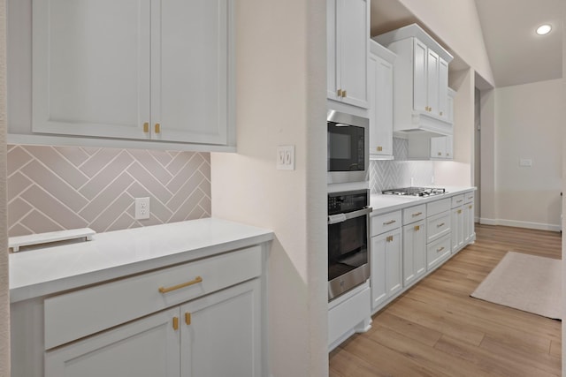 kitchen with white cabinets, under cabinet range hood, stainless steel appliances, light countertops, and light wood-style floors