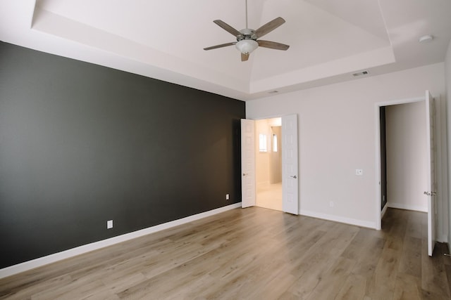 unfurnished room with a ceiling fan, visible vents, baseboards, light wood-type flooring, and a raised ceiling